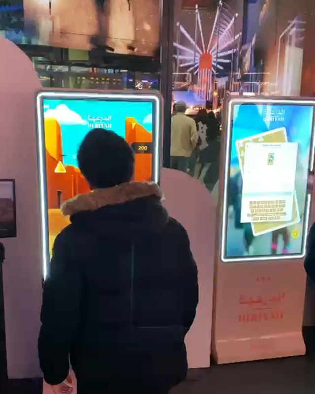 A visitor at the Diriyah stand at Outernet London, between two FRXME displays.